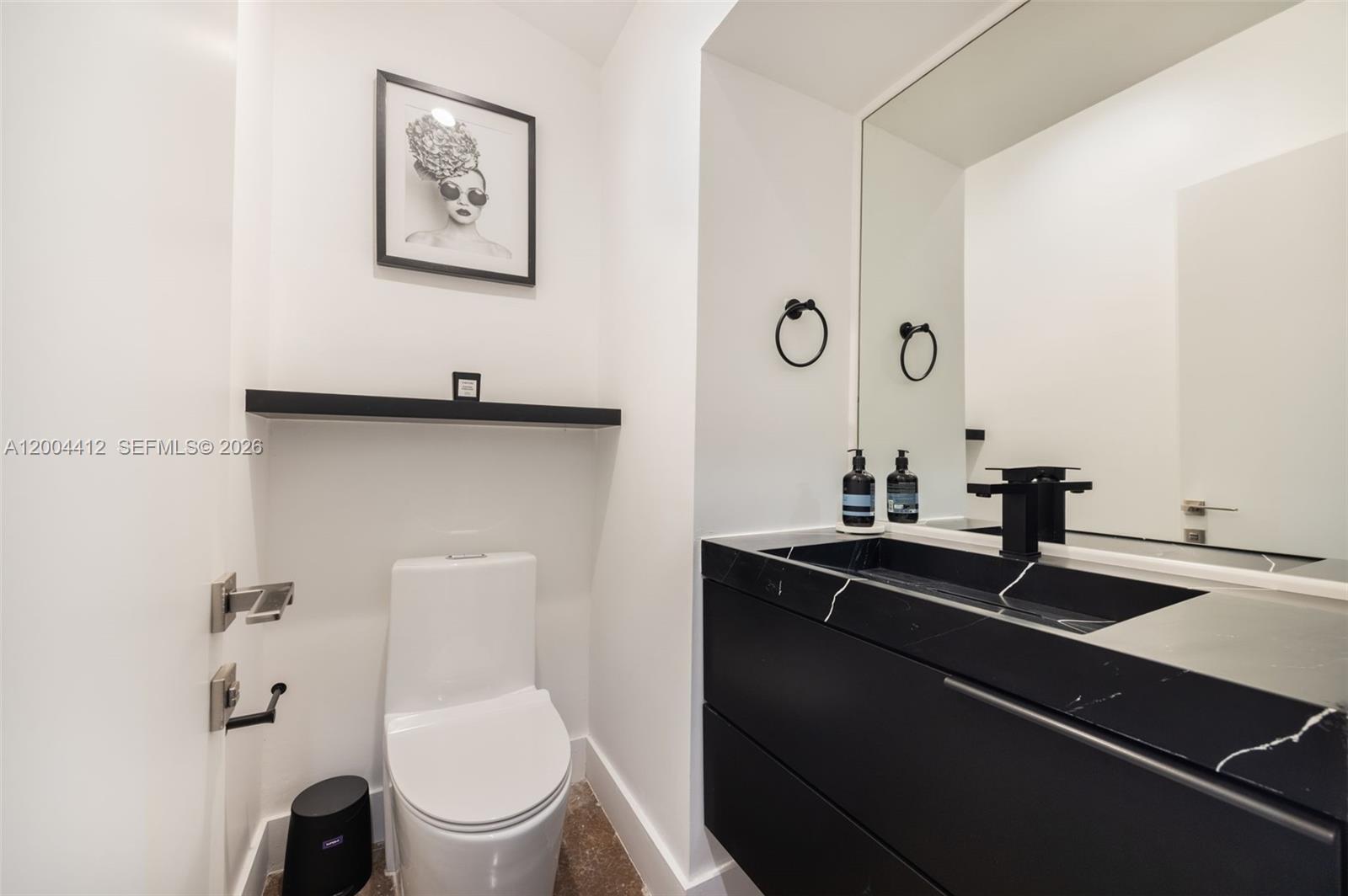 A modern powder room features a black marble vanity, white toilet, and minimalist black accents — 3775 S Le Jeune Rd, Miami FL 33146, MIAMI, FL