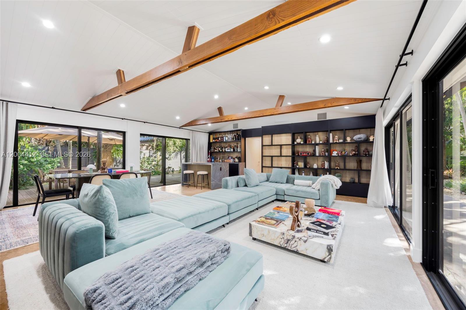 A spacious living room features a large light blue sectional, wooden ceiling beams, and shelving — 3775 S Le Jeune Rd, Miami FL 33146, MIAMI, FL