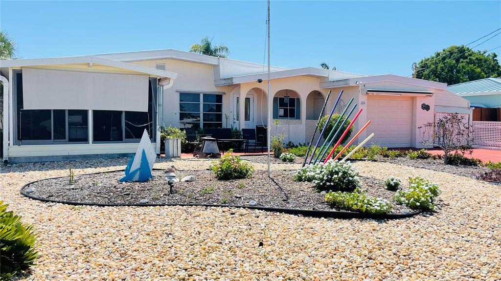 A single-story house with a gravel yard, a covered patio, and colorful decorative garden stakes — 409 BRYN MAWR ISLAND, BRADENTON, FL