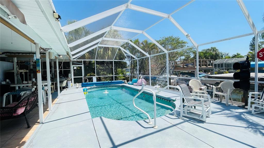 A screened-in swimming pool sits on a concrete patio next to a covered outdoor living area — 409 BRYN MAWR ISLAND, BRADENTON, FL