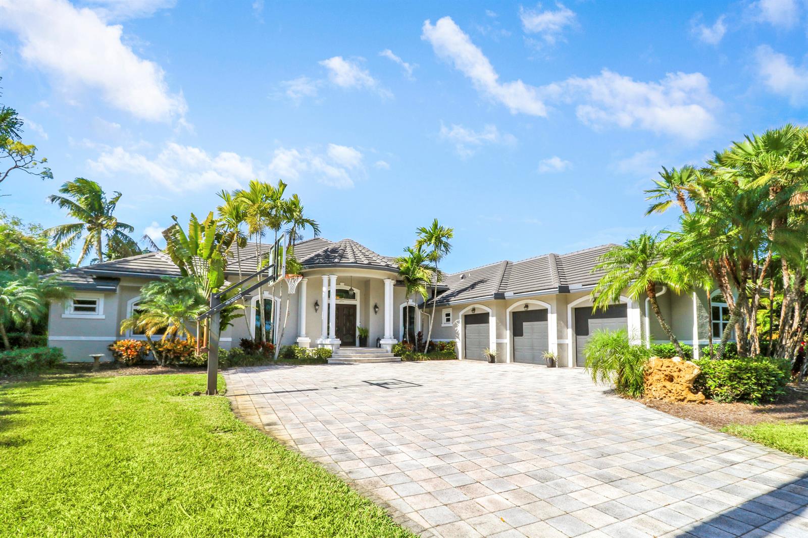 A single-story house with a paved driveway, three-car garage, and palm trees under a blue sky — 18512 SE Old Trail Drive E, Jupiter FL 33478, JUPITER, FL