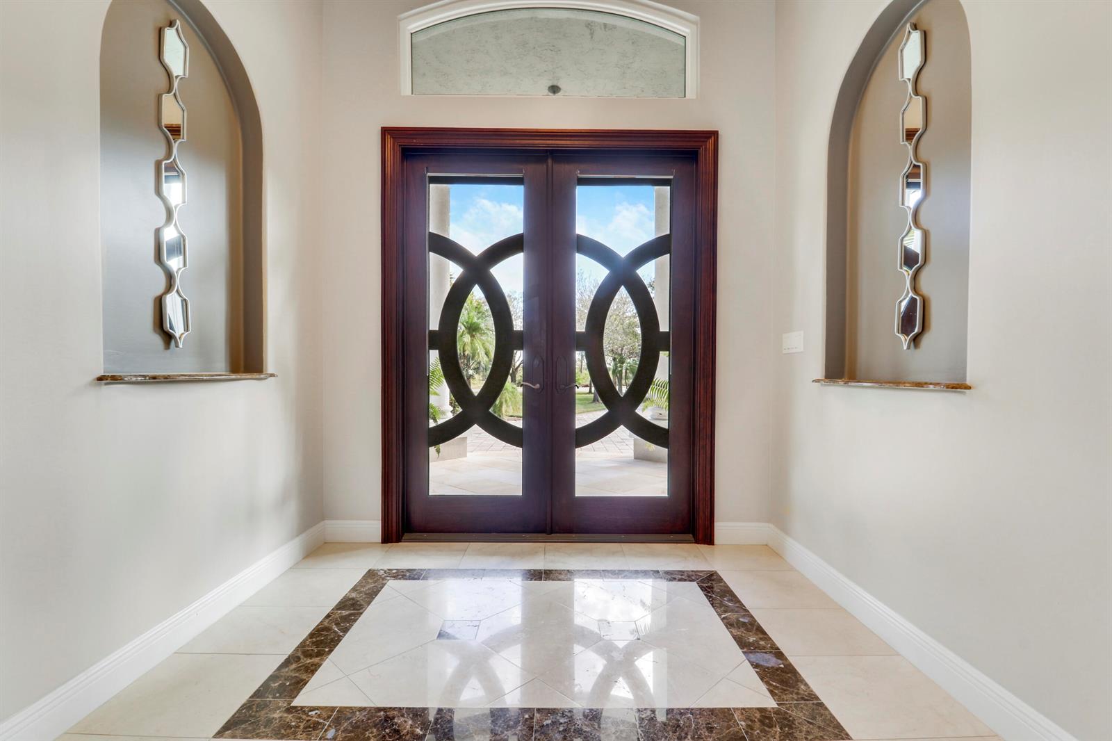 An entryway features a double door with circular glass patterns, arched wall niches, and tiled flooring — 18512 SE Old Trail Drive E, Jupiter FL 33478, JUPITER, FL