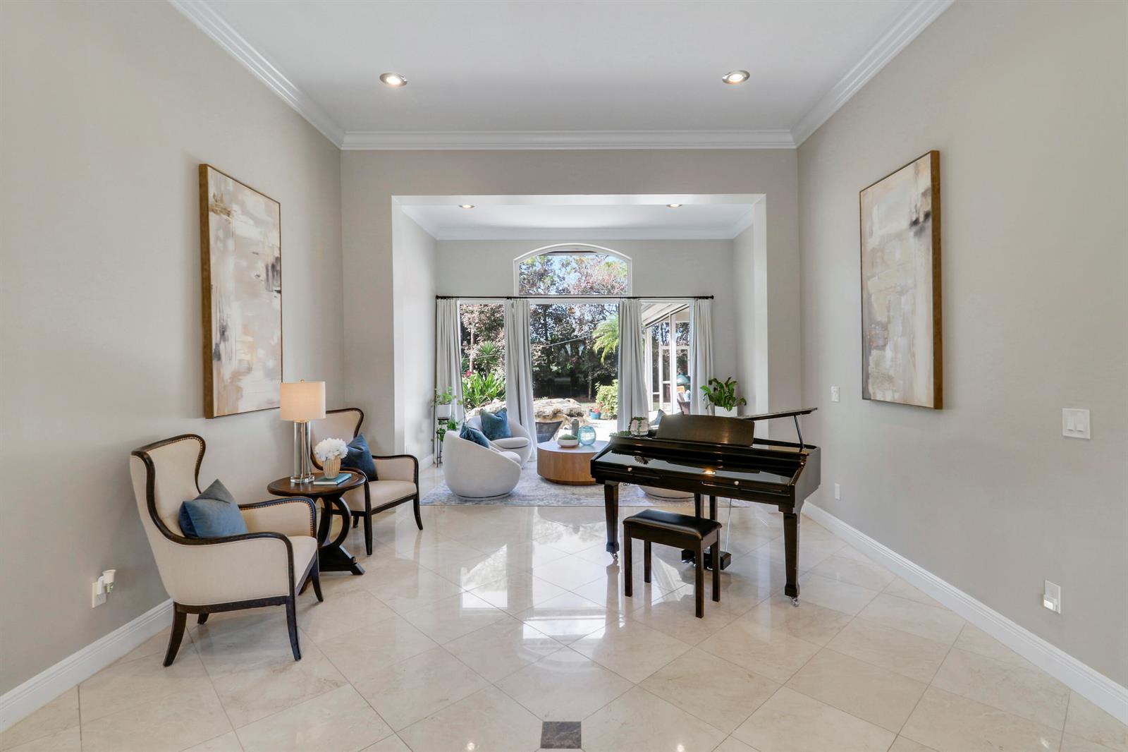 A bright living room features a grand piano, two armchairs, and large glass patio doors — 18512 SE Old Trail Drive E, Jupiter FL 33478, JUPITER, FL