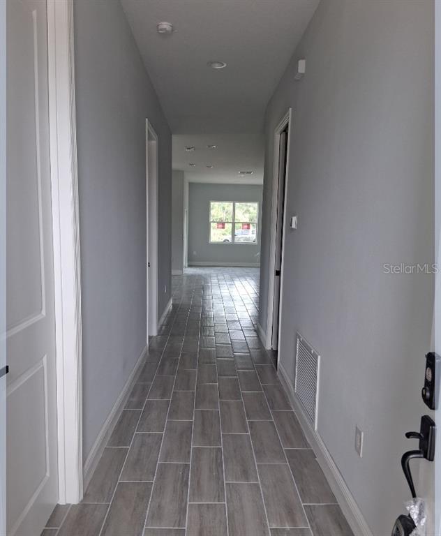 A long hallway with gray walls and wood-look tile flooring leads toward a bright room — 799 SW WHITE CLOUD STREET SW, PALM BAY, FL