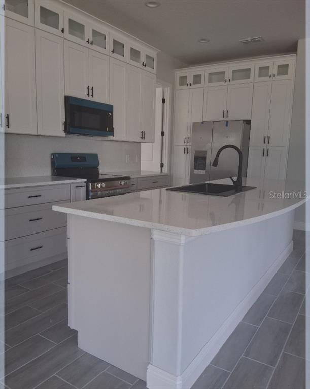 A modern kitchen features white cabinetry, a central island with a sink, and gray flooring — 799 SW WHITE CLOUD STREET SW, PALM BAY, FL