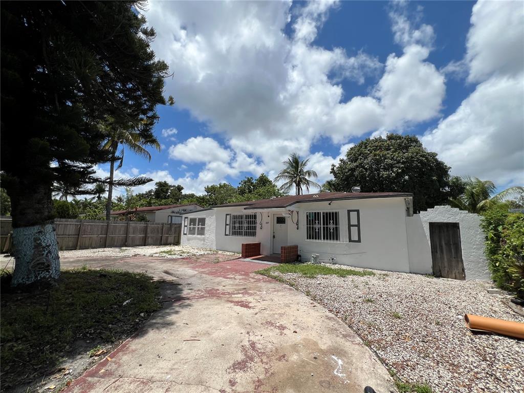 A single-story white house with a concrete driveway and a wooden fence under a cloudy sky — 845 NW 130TH STREET, NORTH MIAMI, FL