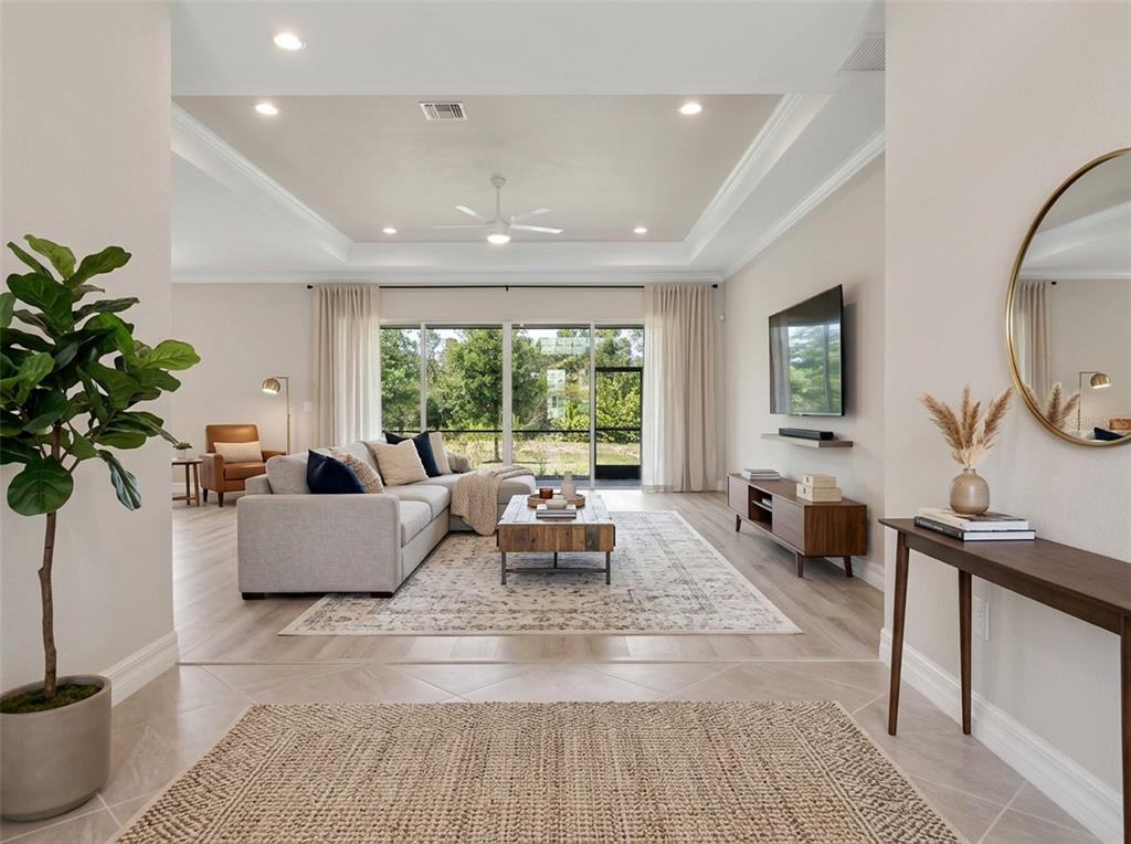 A spacious living room features a tray ceiling, light wood flooring, and a large sectional sofa — 14500 PONCE DE LEON TRAIL, PORT CHARLOTTE, FL
