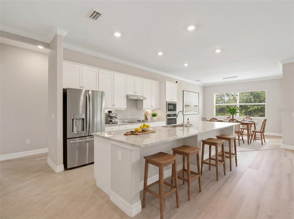 A modern kitchen features white cabinets, a granite island with bar stools, and stainless appliances — 14500 PONCE DE LEON TRAIL, PORT CHARLOTTE, FL