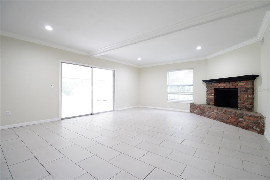 An empty living room features white tile flooring, a brick fireplace, and sliding glass doors — 10907 SW 24TH AVENUE, GAINESVILLE, FL