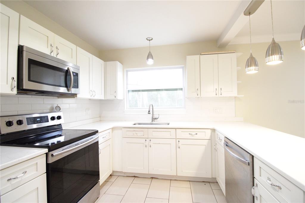 A kitchen with white cabinets, stainless steel appliances, a window, and light-colored tile flooring — 10907 SW 24TH AVENUE, GAINESVILLE, FL