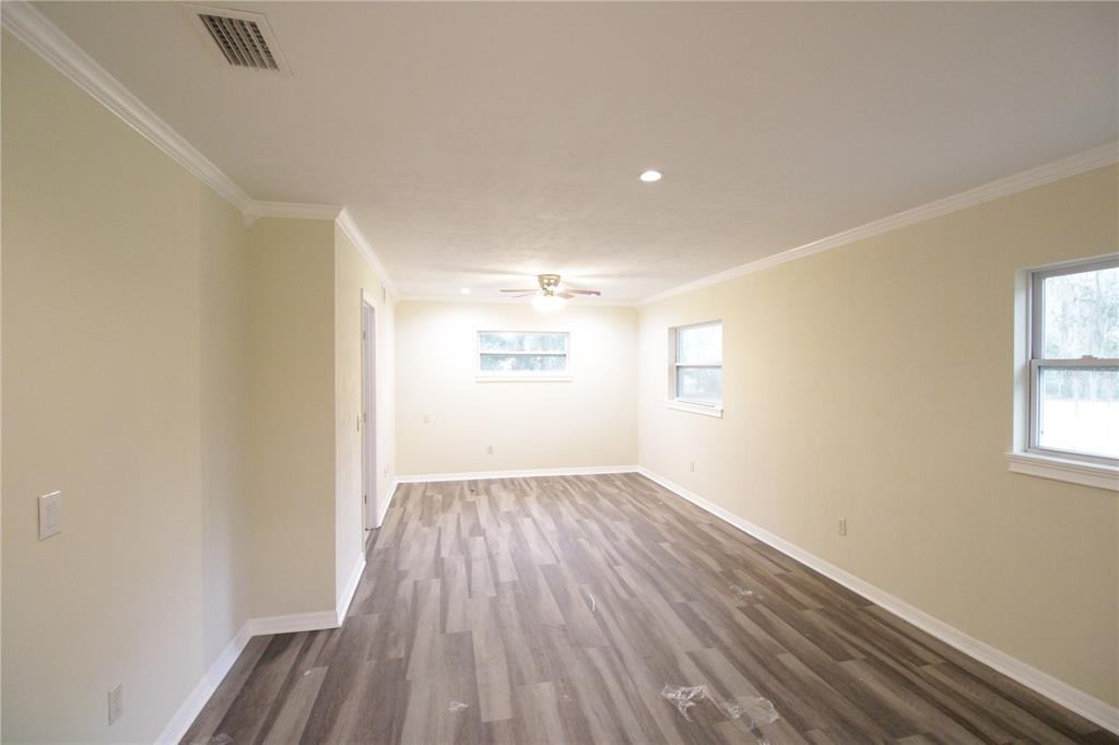 An empty room with light-colored walls, crown molding, and wood-look vinyl plank flooring — 10907 SW 24TH AVENUE, GAINESVILLE, FL