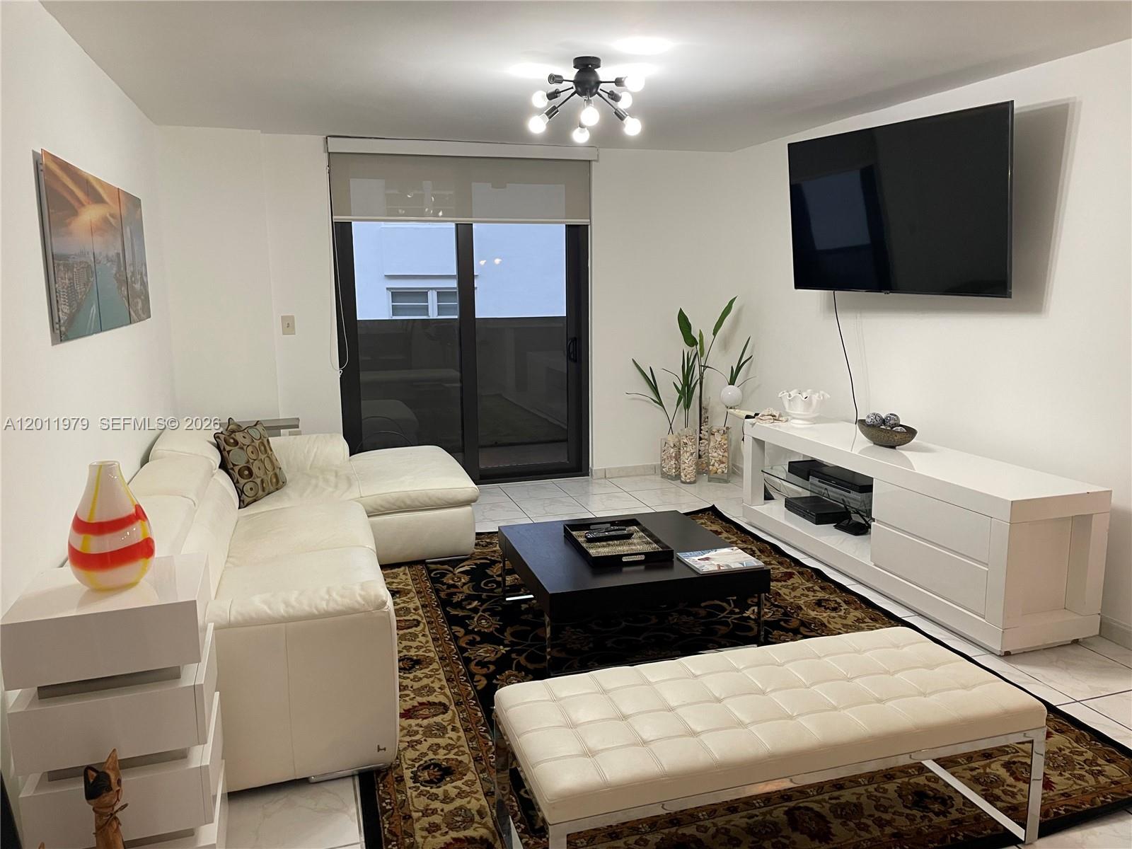A living room features a white sectional sofa, a dark coffee table, and a television — 1621 Collins Ave # 707, Miami Beach FL 33139, MIAMI BEACH, FL