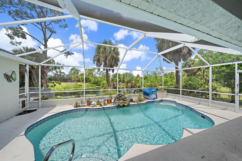 A screened-in pool patio features a small waterfall, potted plants, and a view of greenery — 1687 WISE DRIVE, NORTH PORT, FL