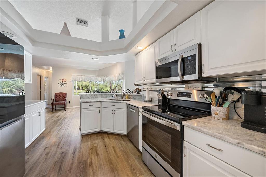 A kitchen features white cabinets, stainless steel appliances, and wood-look flooring under a tray ceiling — 1687 WISE DRIVE, NORTH PORT, FL