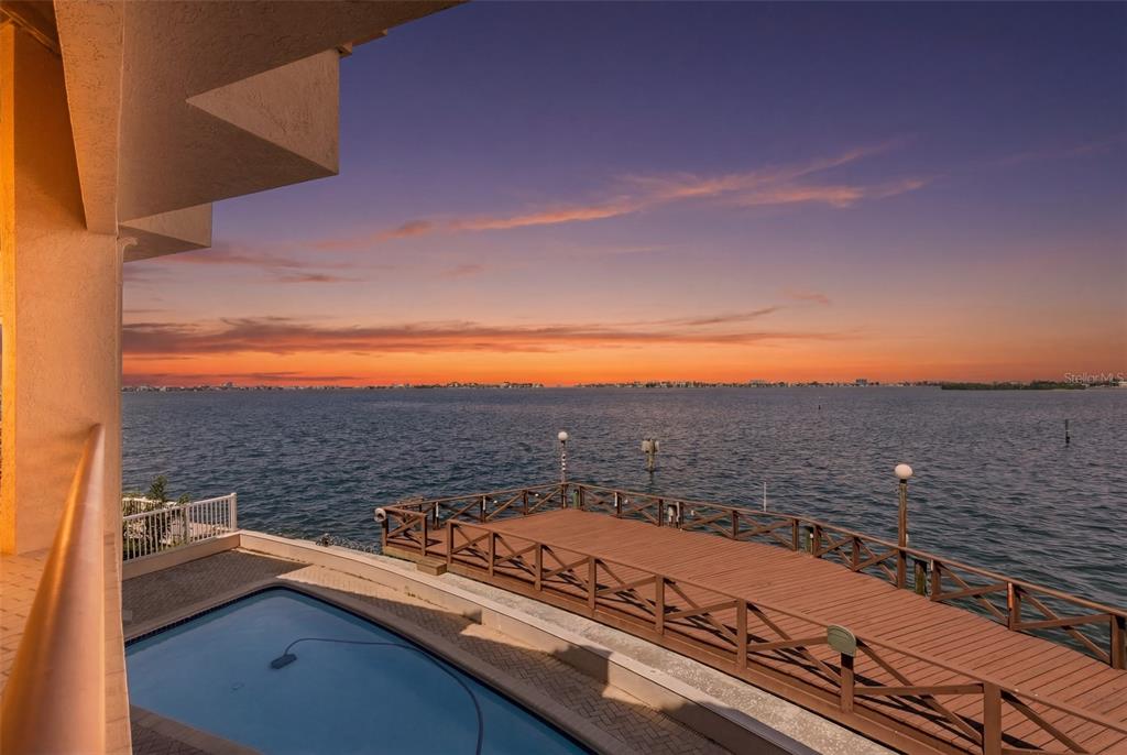 A swimming pool and wooden deck overlook a large body of water at sunset — 2869 SEABREEZE DRIVE S, GULFPORT, FL