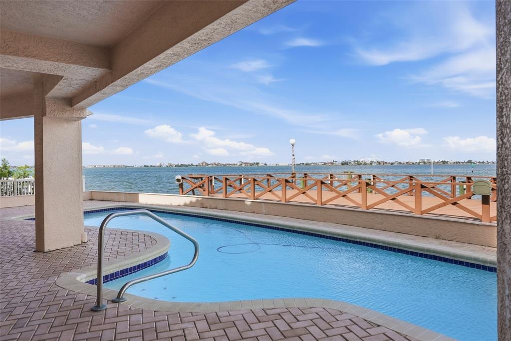 A swimming pool sits on a paved patio overlooking a bay with a wooden railing — 2869 SEABREEZE DRIVE S, GULFPORT, FL