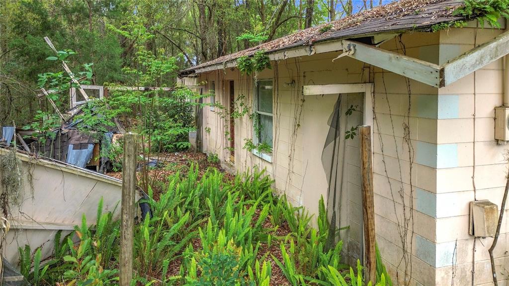 An exterior view of a dilapidated, single-story concrete block house surrounded by overgrown vegetation — 10160 SE 49TH COURT, BELLEVIEW, FL