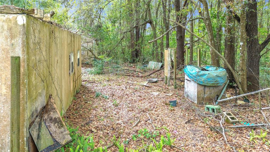 An exterior view of a weathered concrete structure surrounded by trees and overgrown yard debris — 10160 SE 49TH COURT, BELLEVIEW, FL