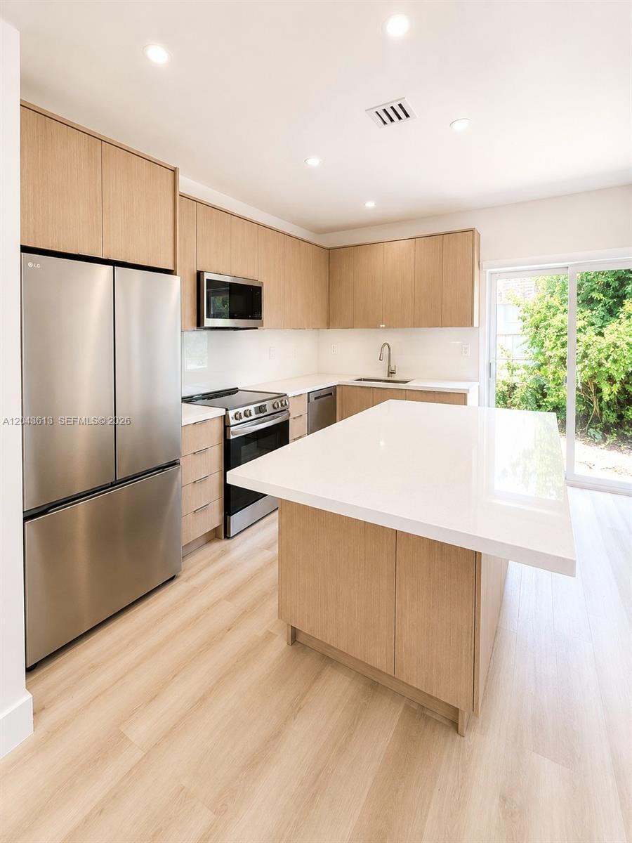 A modern kitchen features light wood cabinetry, stainless steel appliances, and a white quartz island — 1627 N 28th Ct, Hollywood FL 33020, HOLLYWOOD, FL