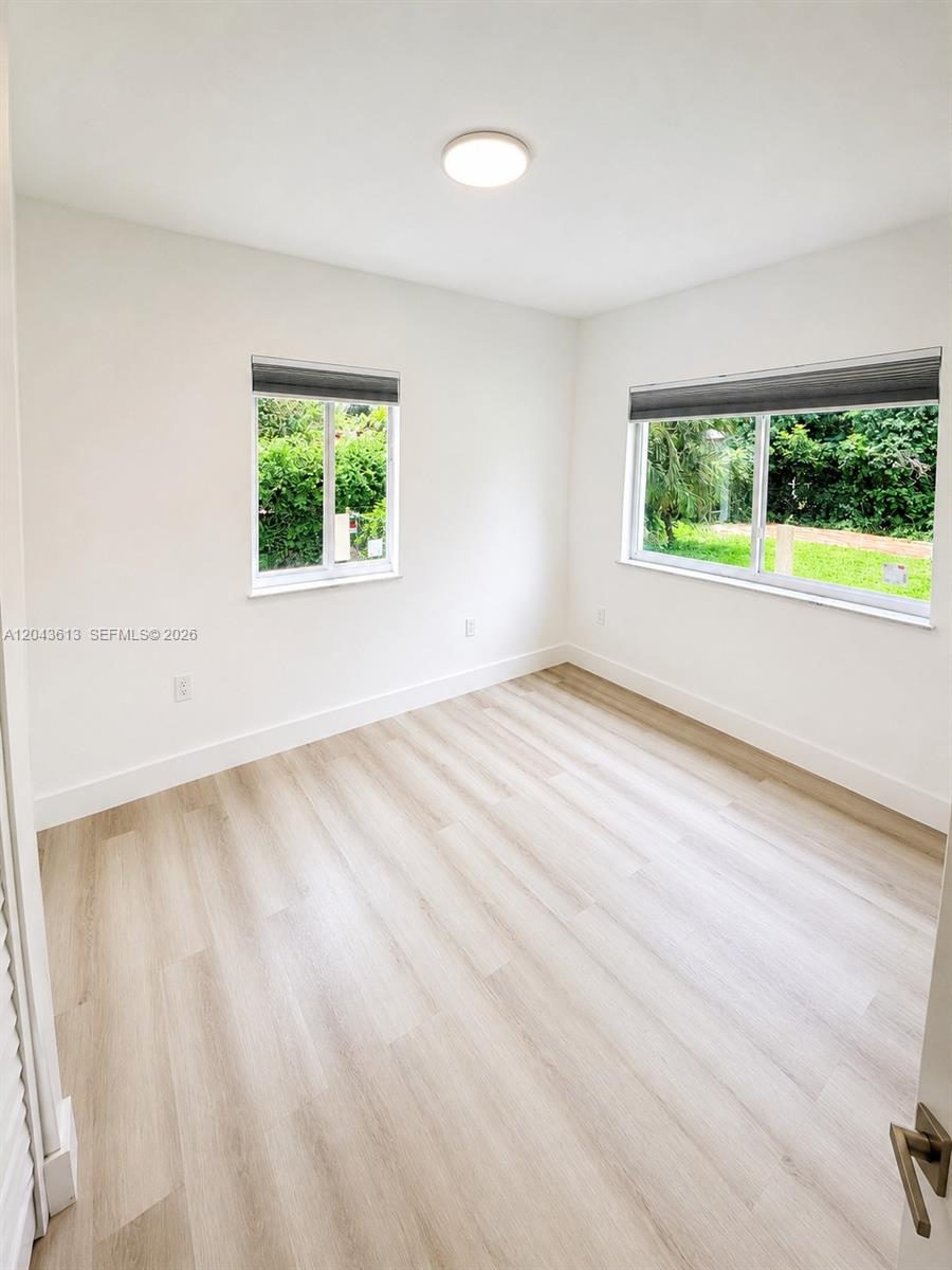 An empty room features light wood-look flooring, white walls, and two windows with blinds — 1627 N 28th Ct, Hollywood FL 33020, HOLLYWOOD, FL
