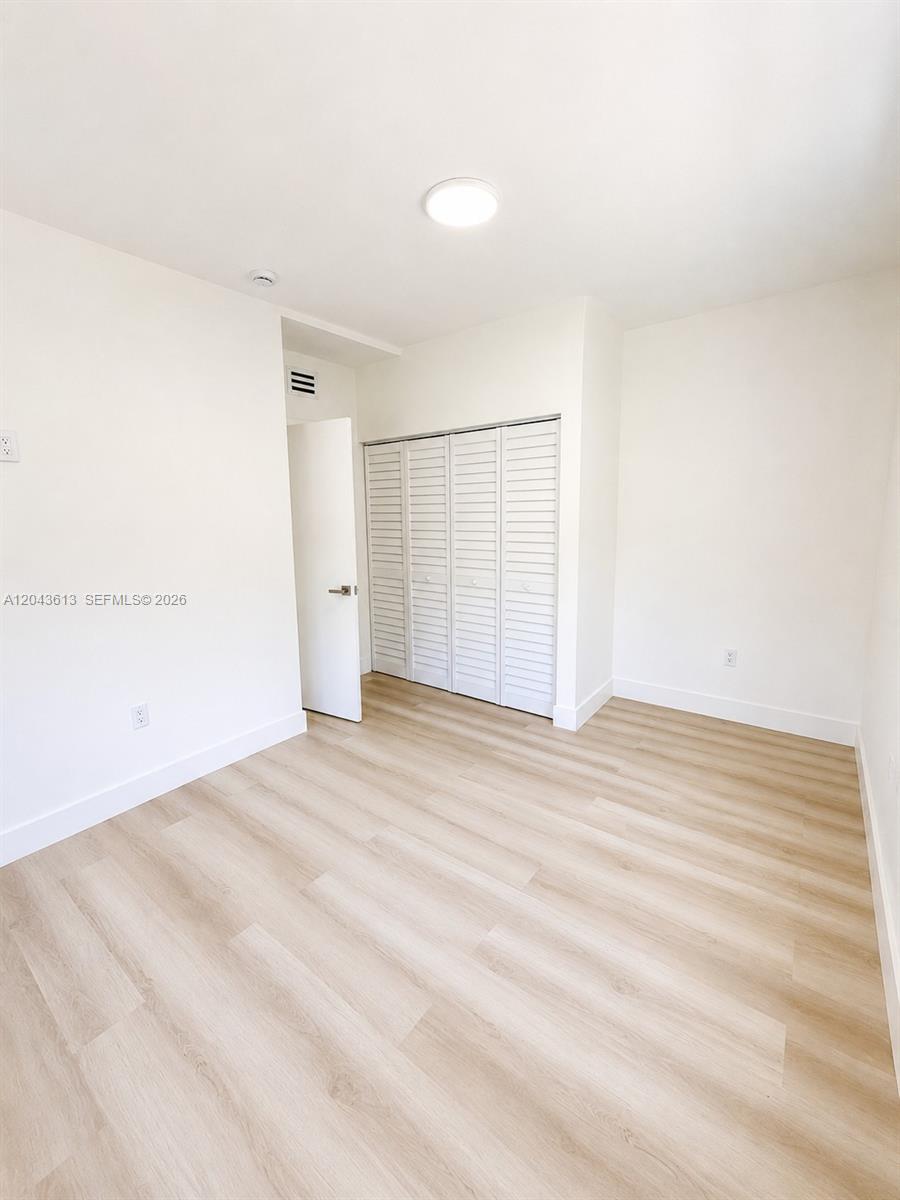 An empty bedroom features light wood-look flooring, white walls, and a white louvered closet — 1627 N 28th Ct, Hollywood FL 33020, HOLLYWOOD, FL