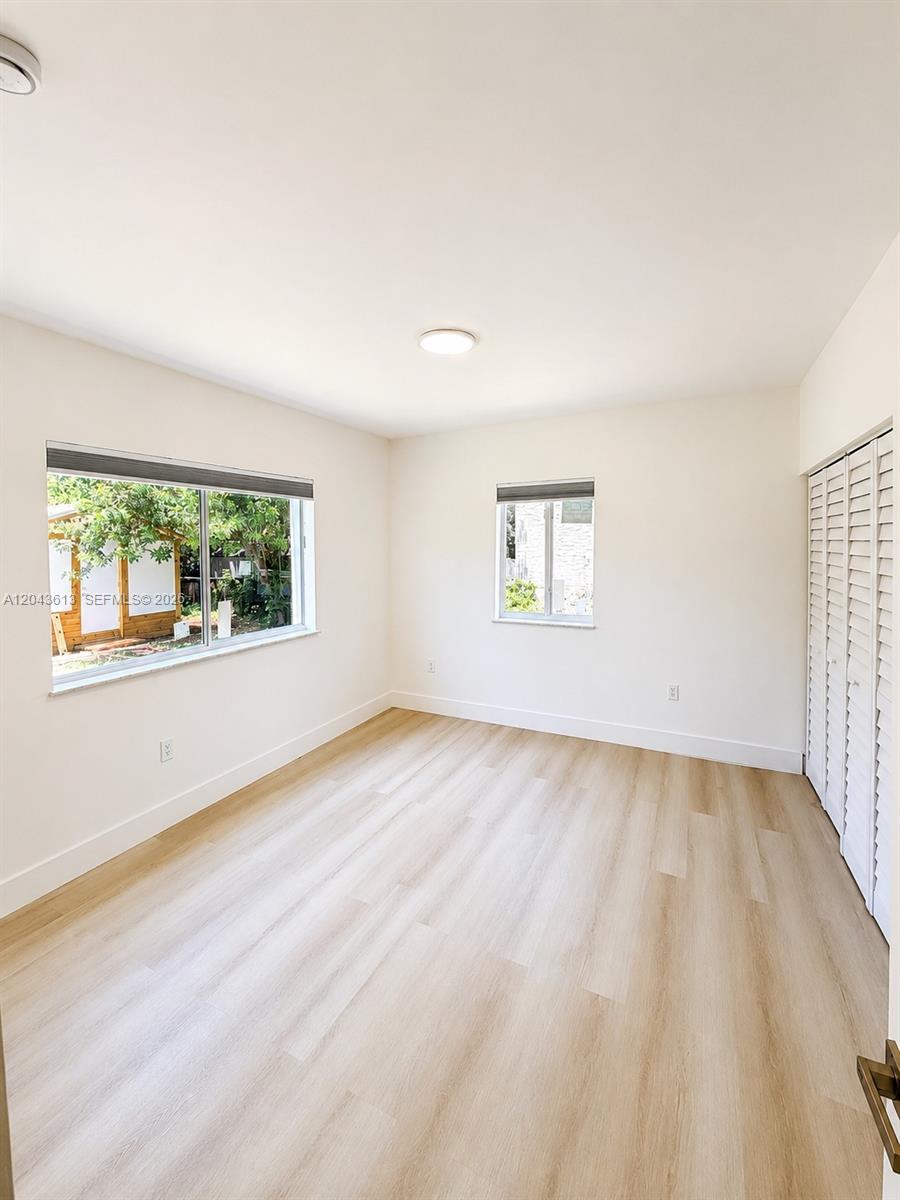 An empty bedroom features light wood-look flooring, white walls, two windows, and louvered closet doors — 1627 N 28th Ct, Hollywood FL 33020, HOLLYWOOD, FL