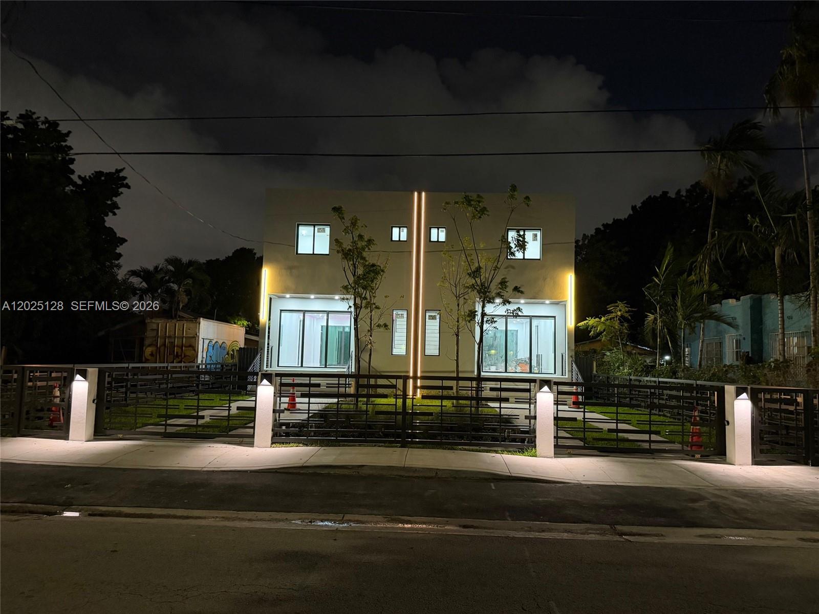 A modern two-story duplex at night with illuminated exterior lighting and a black metal fence — 1924 NW 27th St, Miami FL 33142, MIAMI, FL