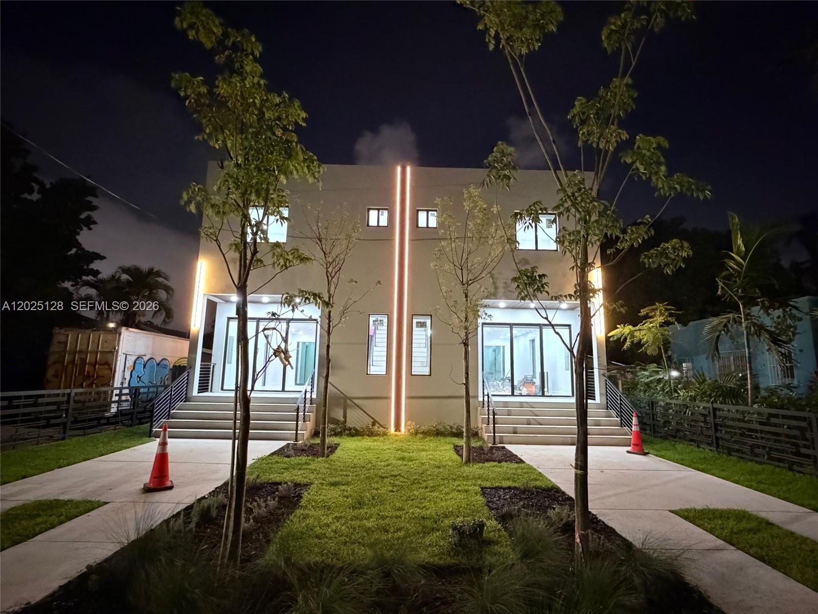 A modern two-story duplex exterior features illuminated vertical accents, glass entryways, and concrete stairs — 1924 NW 27th St, Miami FL 33142, MIAMI, FL