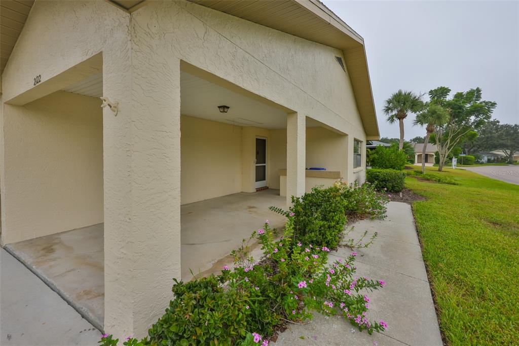 A covered concrete entryway with a beige stucco exterior and pink flowering bushes — 2122 HEREFORD DRIVE UNIT 511, SUN CITY CENTER, FL