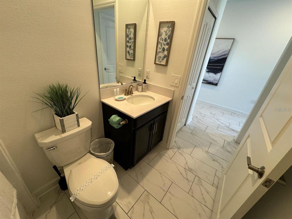 A bathroom features a dark vanity, white countertop, toilet, and light-colored marble-look floor tiles — 9235 SOMMERSET HILLS DRIVE, DAVENPORT, FL