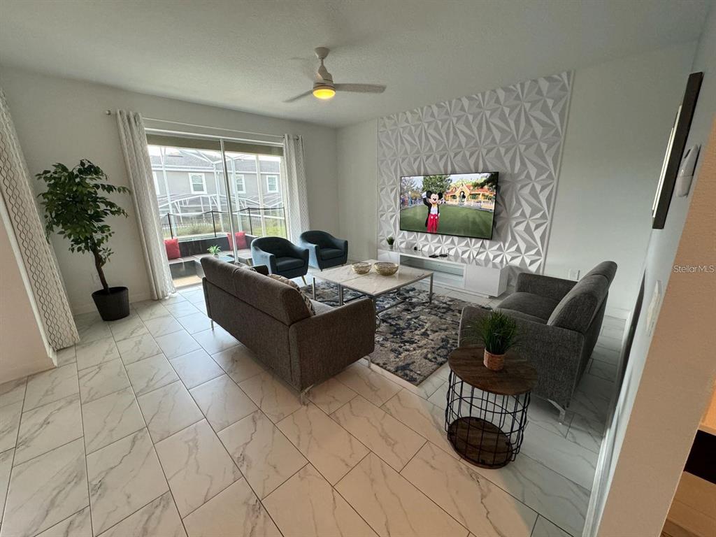 A living room features gray sofas, a patterned area rug, and a geometric accent wall — 9235 SOMMERSET HILLS DRIVE, DAVENPORT, FL