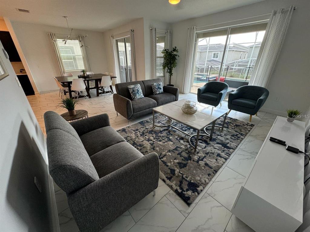 A living room with gray sofas, a patterned rug, and a dining area in the background — 9235 SOMMERSET HILLS DRIVE, DAVENPORT, FL