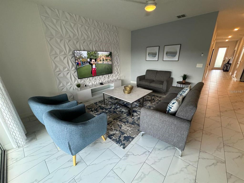 A living room features a textured accent wall, a television, and gray and blue furniture — 9235 SOMMERSET HILLS DRIVE, DAVENPORT, FL