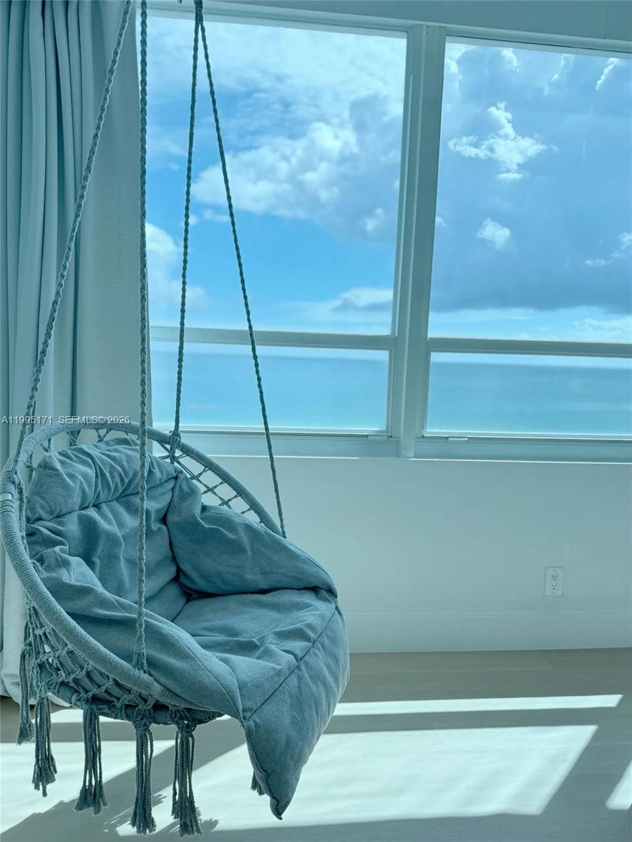 A hanging chair sits in a room with large windows overlooking the ocean — 5445 Collins Ave # 635, Miami Beach FL 33140, MIAMI BEACH, FL