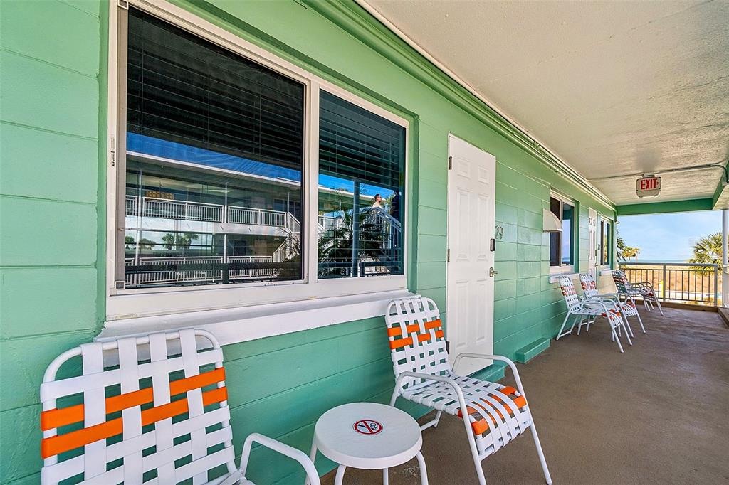 An outdoor walkway with mint green walls, white doors, and several patio chairs — 11730 GULF BOULEVARD UNIT 29, TREASURE ISLAND, FL