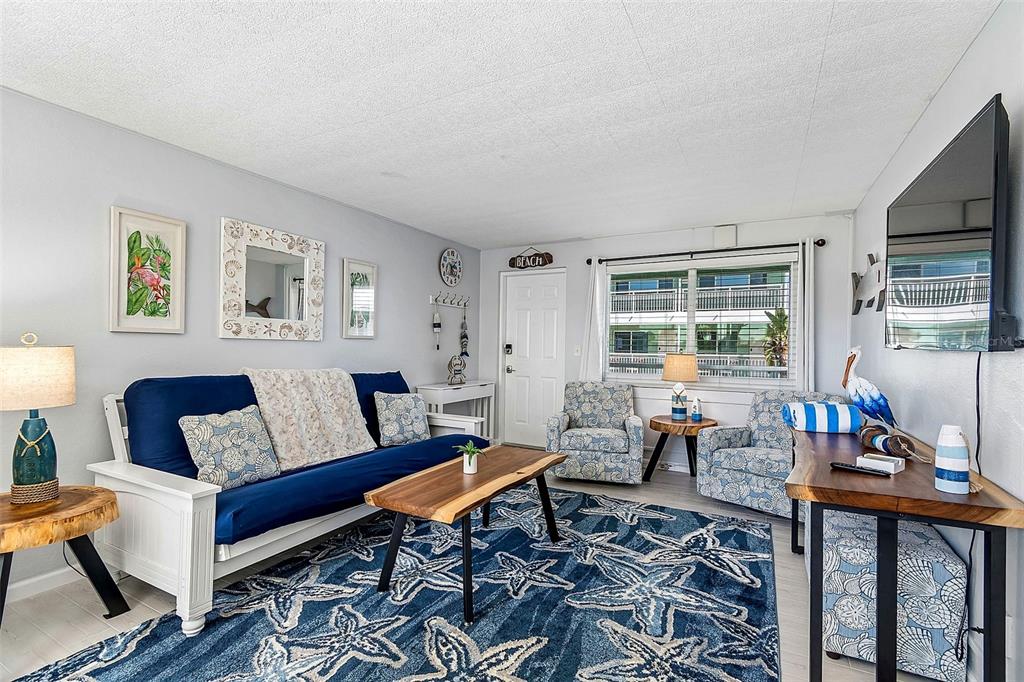A living room features a blue futon, a starfish-patterned rug, and a wooden coffee table — 11730 GULF BOULEVARD UNIT 29, TREASURE ISLAND, FL