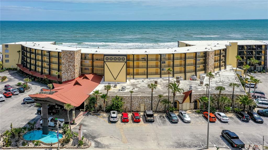 An aerial view shows a multi-story, curved beachfront hotel with a red roof and parking — 2301 S ATLANTIC AVENUE UNIT 126, DAYTONA BEACH, FL