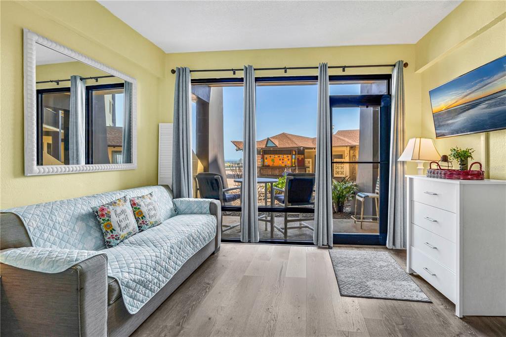 A living room with a sofa, white dresser, and large windows overlooking an outdoor patio — 2301 S ATLANTIC AVENUE UNIT 126, DAYTONA BEACH, FL