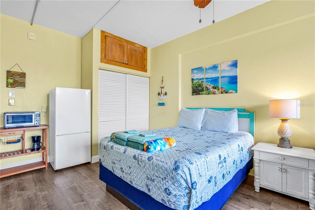 A bedroom features a bed with a patterned quilt, a white refrigerator, and a nightstand — 2301 S ATLANTIC AVENUE UNIT 126, DAYTONA BEACH, FL
