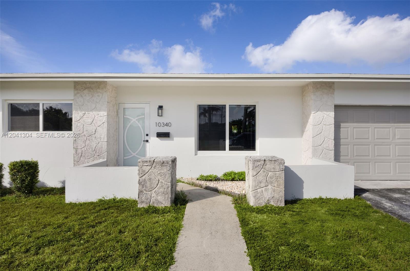 A white house exterior features stone accents, a modern front door, and a concrete walkway — 10340 SW 157th St, Miami FL 33157, MIAMI, FL
