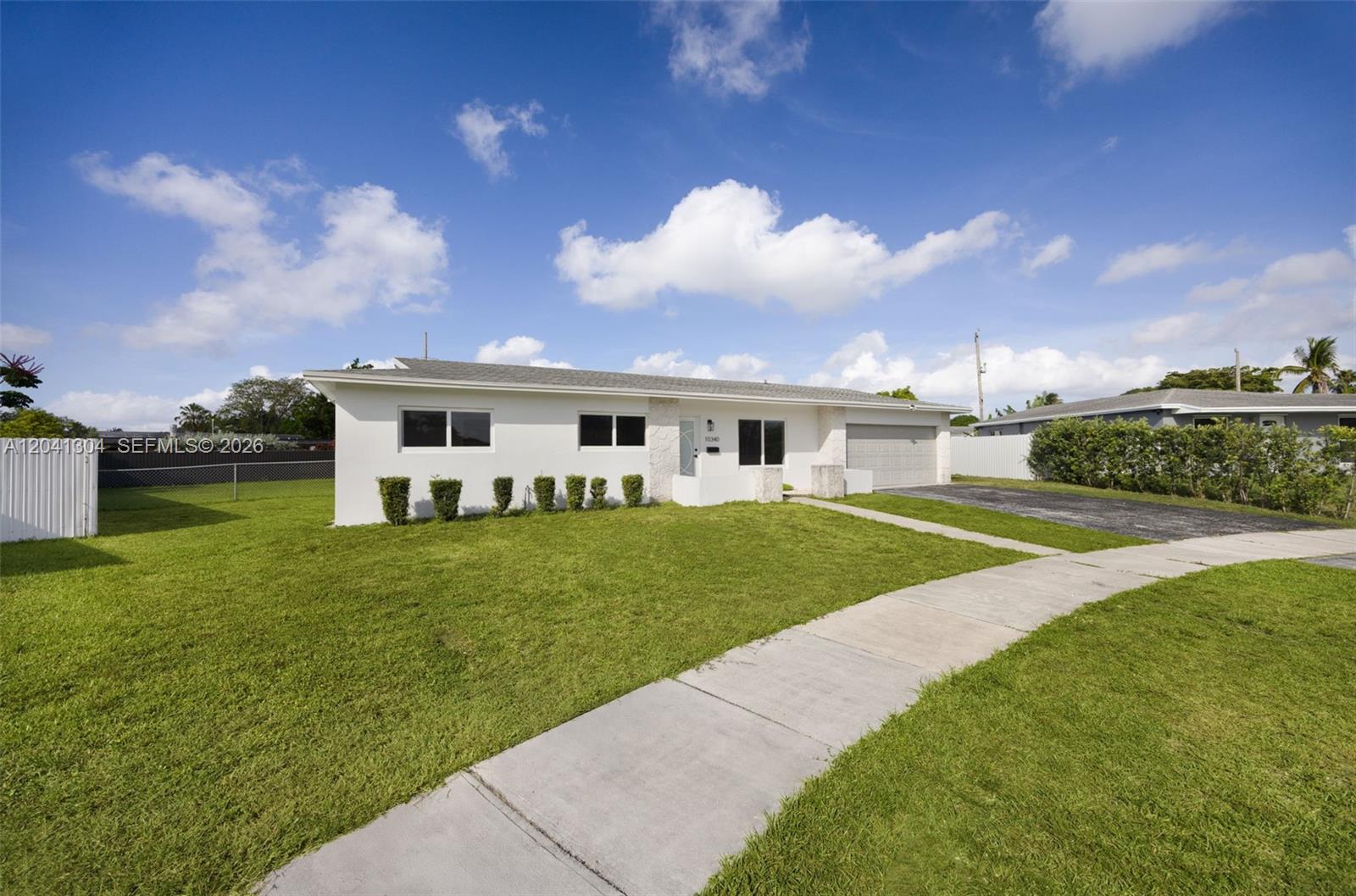 A white, single-story house with a garage and a front lawn under a blue sky — 10340 SW 157th St, Miami FL 33157, MIAMI, FL