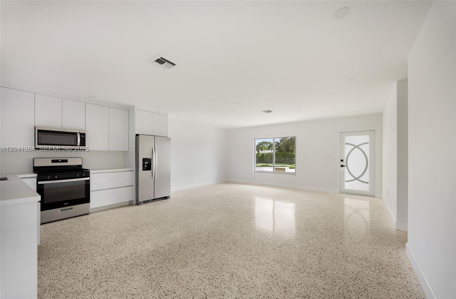 A modern kitchen with white cabinets and stainless steel appliances opens into a spacious room — 10340 SW 157th St, Miami FL 33157, MIAMI, FL