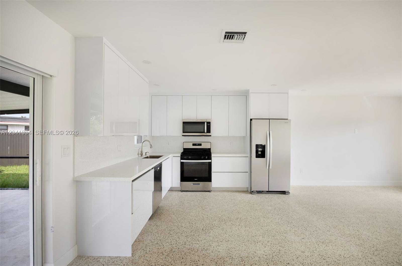 A modern kitchen features white flat-panel cabinets, stainless steel appliances, and speckled flooring — 10340 SW 157th St, Miami FL 33157, MIAMI, FL
