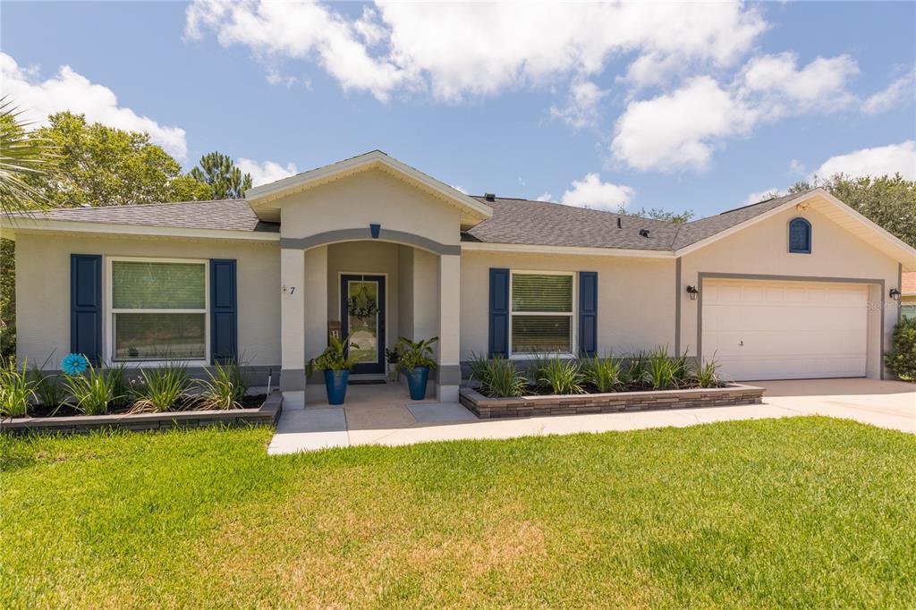 A single-story house with a light-colored stucco exterior, blue shutters, and a two-car garage — 7 LANCASTER LANE, PALM COAST, FL