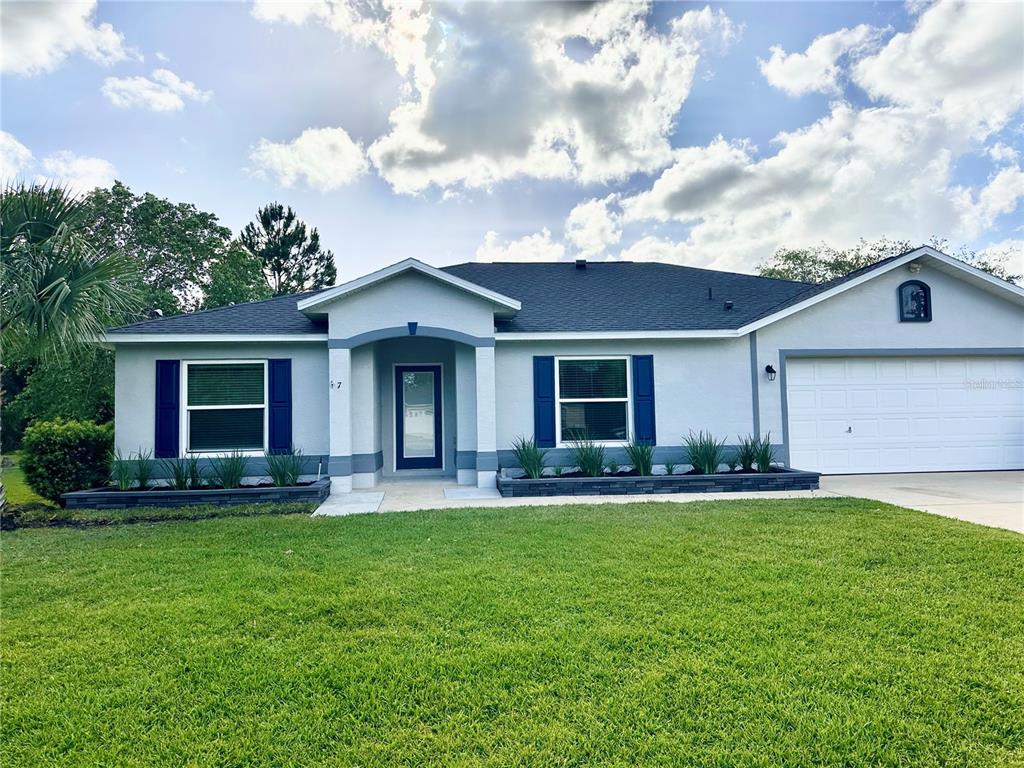 A single-story house with a white garage, blue shutters, and a covered front entryway — 7 LANCASTER LANE, PALM COAST, FL