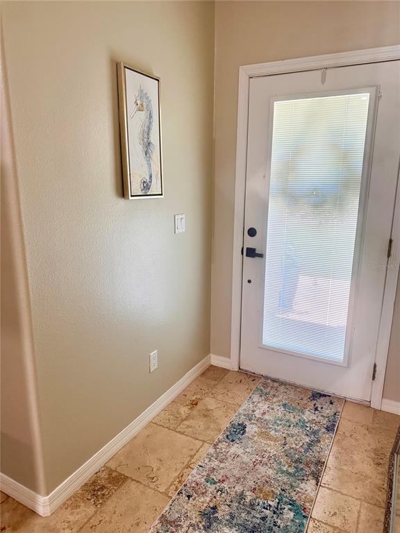 An entryway features travertine tile flooring, a seahorse wall art piece, and a glass-paneled door — 7 LANCASTER LANE, PALM COAST, FL