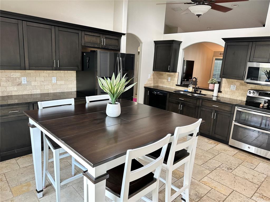 A kitchen features dark wood cabinets, a central dining table, and light-colored stone tile flooring — 7 LANCASTER LANE, PALM COAST, FL