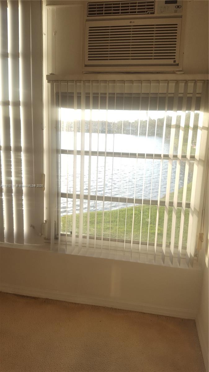 A room with beige carpet features a window covered by vertical blinds overlooking a lake — 19080 NE 3rd Ct # 318, Miami FL 33179, MIAMI, FL