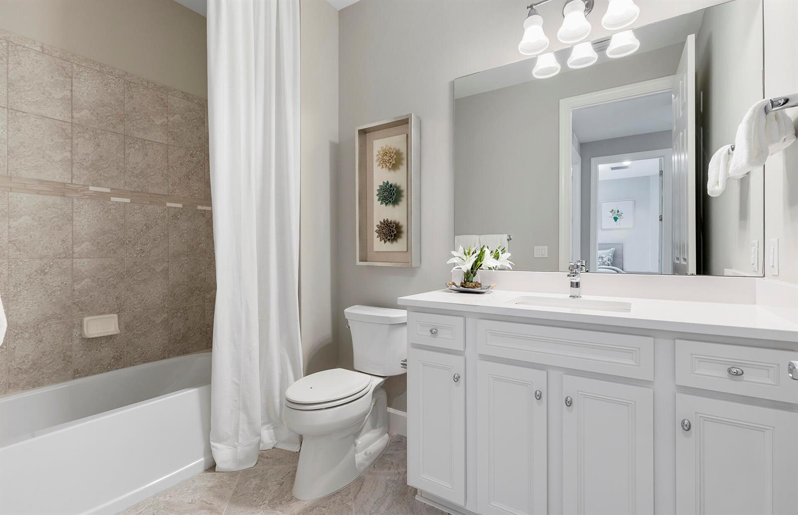 A bathroom features a white vanity, a toilet, and a bathtub with a shower curtain — 6431 Memorial Lane, Ave Maria FL 34142, AVE MARIA, FL