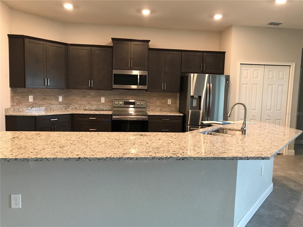 A kitchen features dark wood cabinets, granite countertops, stainless steel appliances, and a breakfast bar — 1437 CYPRESS VIEW LANE, LAKELAND, FL